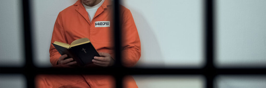 partial image of a prisoner behind bars, reading a book